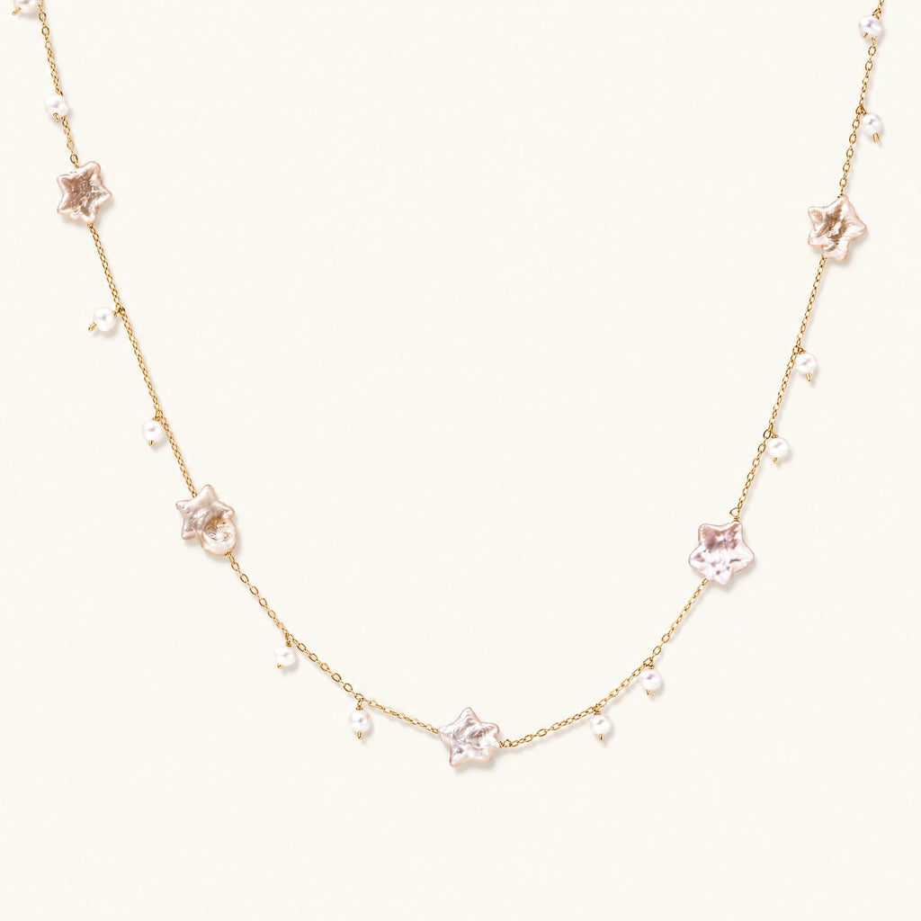 Gold vermeil chain with iridescent star-shaped baroque pearls and small round freshwater pearl drops on cream background.