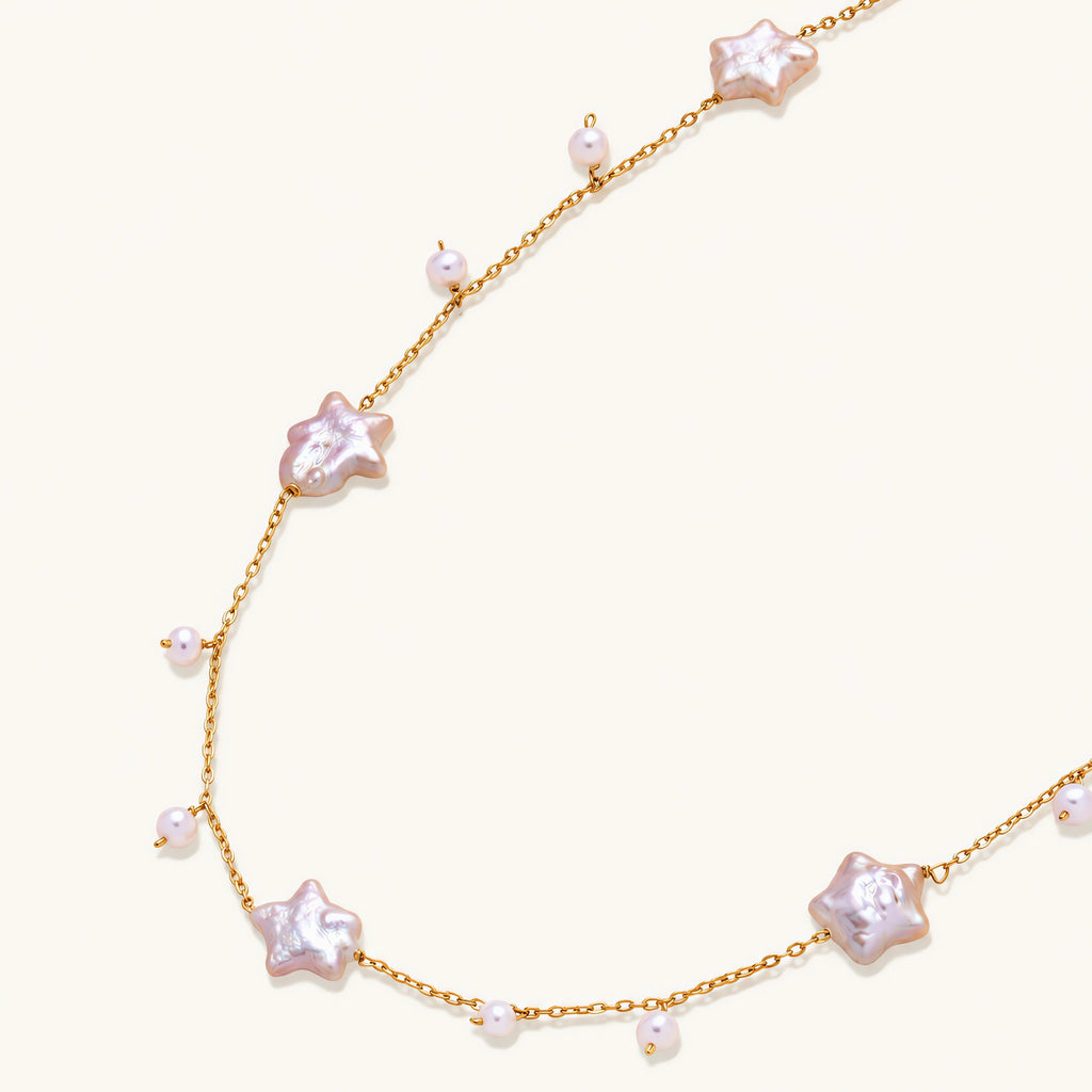 Gold vermeil chain with iridescent star-shaped baroque pearls and small round freshwater pearl drops on cream background.