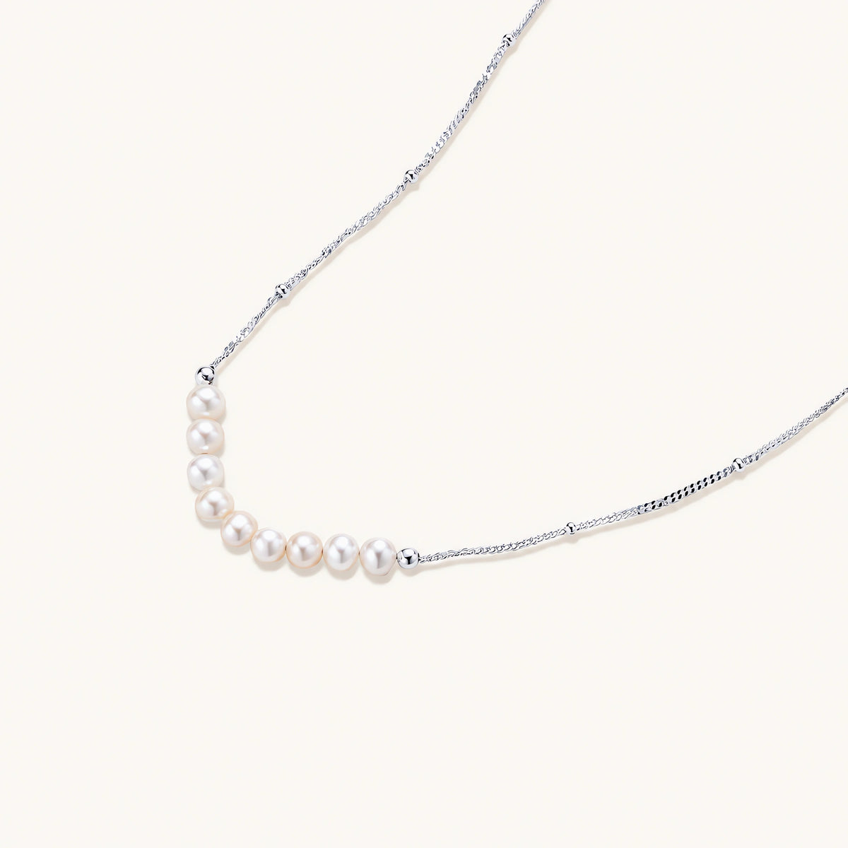 Delicate sterling silver chain necklace with small freshwater pearls arranged in a curved smile arc on cream background.
