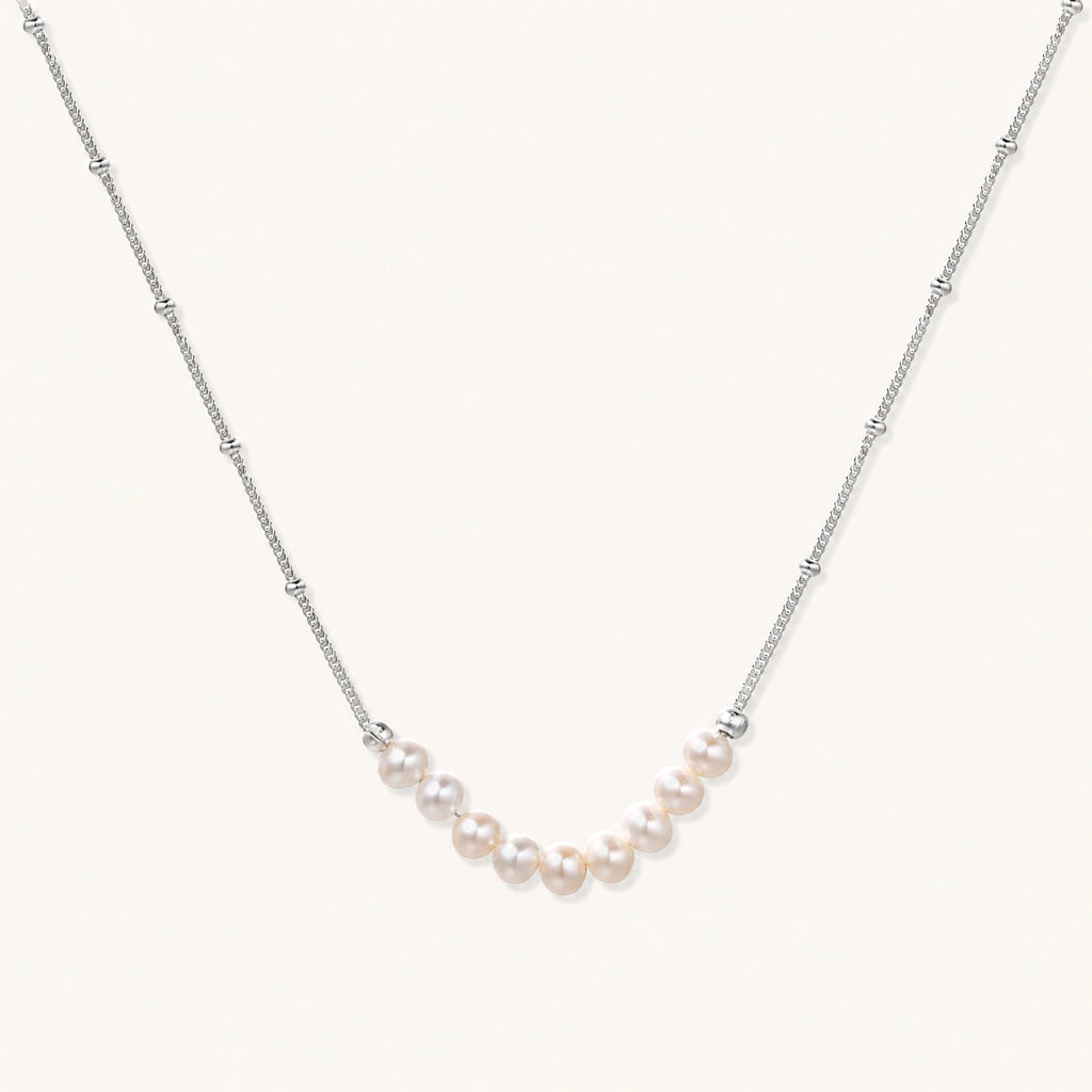 Delicate sterling silver chain necklace with small freshwater pearls arranged in a curved smile arc on cream background.