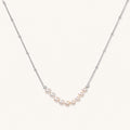 Delicate sterling silver chain necklace with small freshwater pearls arranged in a curved smile arc on cream background.