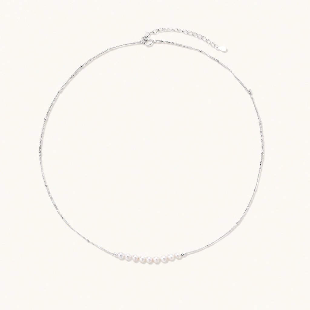 Delicate sterling silver chain necklace with small freshwater pearls arranged in a curved smile arc on cream background.