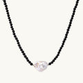 Beaded black agate necklace with iridescent baroque freshwater pearl centerpiece on cream background.