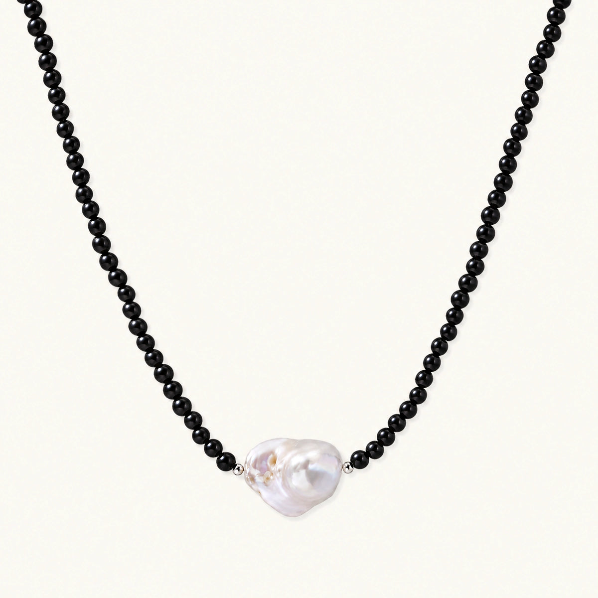 Beaded black agate necklace with iridescent baroque freshwater pearl centerpiece on cream background.