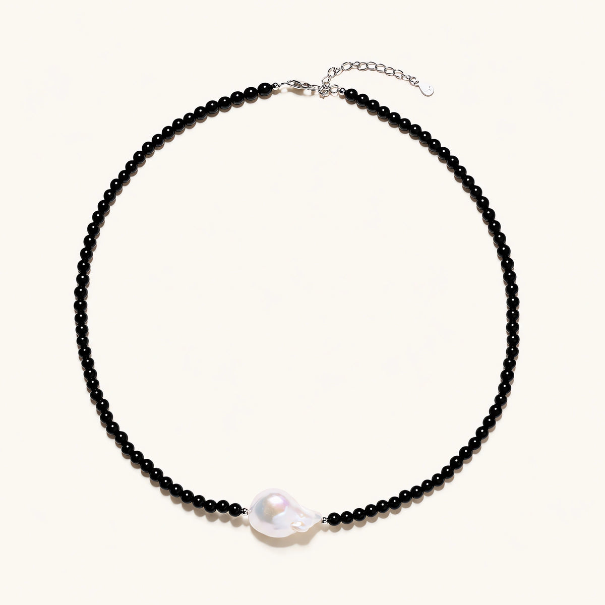 Beaded black agate necklace with iridescent baroque freshwater pearl centerpiece on cream background.