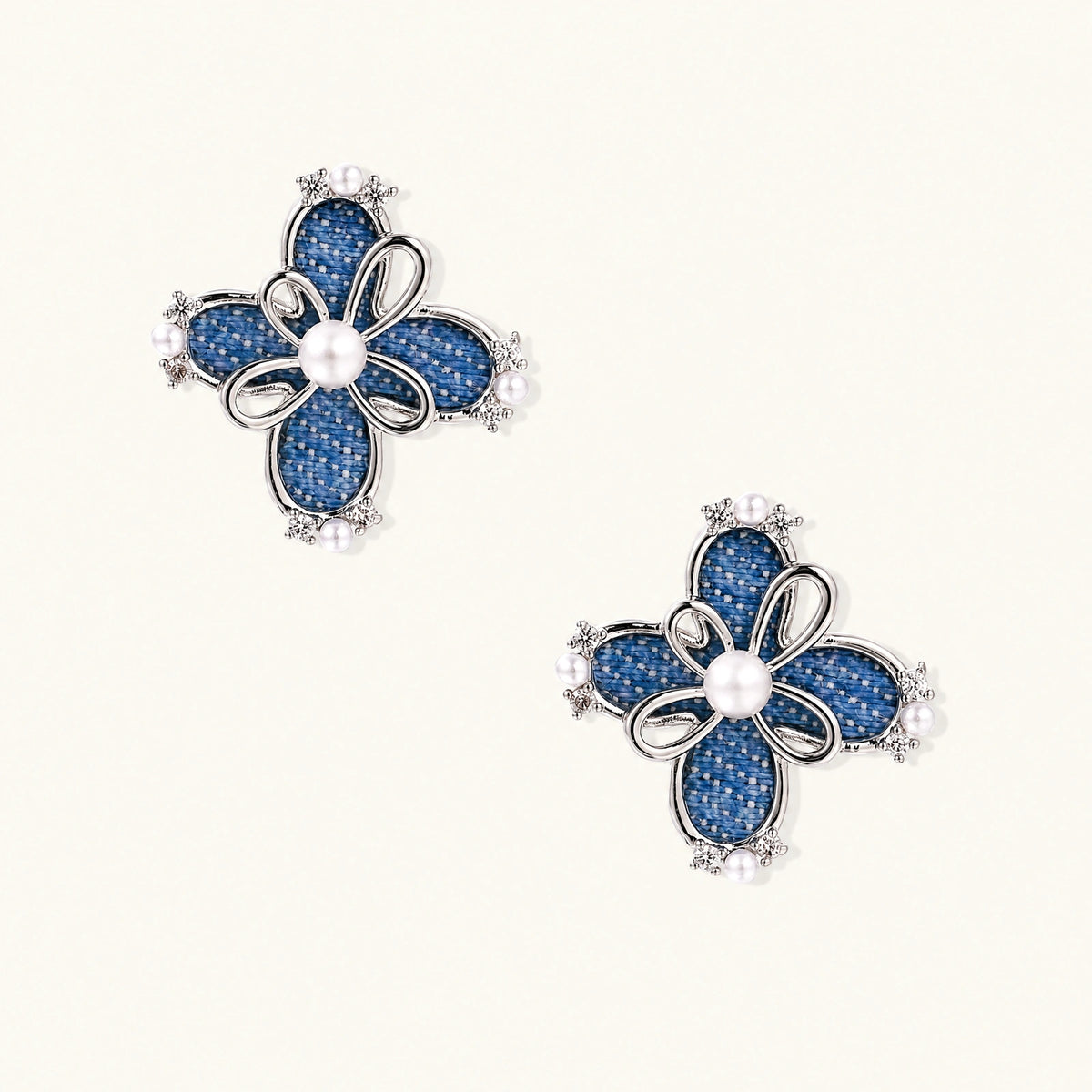 Pair of silver-tone four-petal flower stud earrings with blue denim fabric petals, a center white bead and zirconia accents.