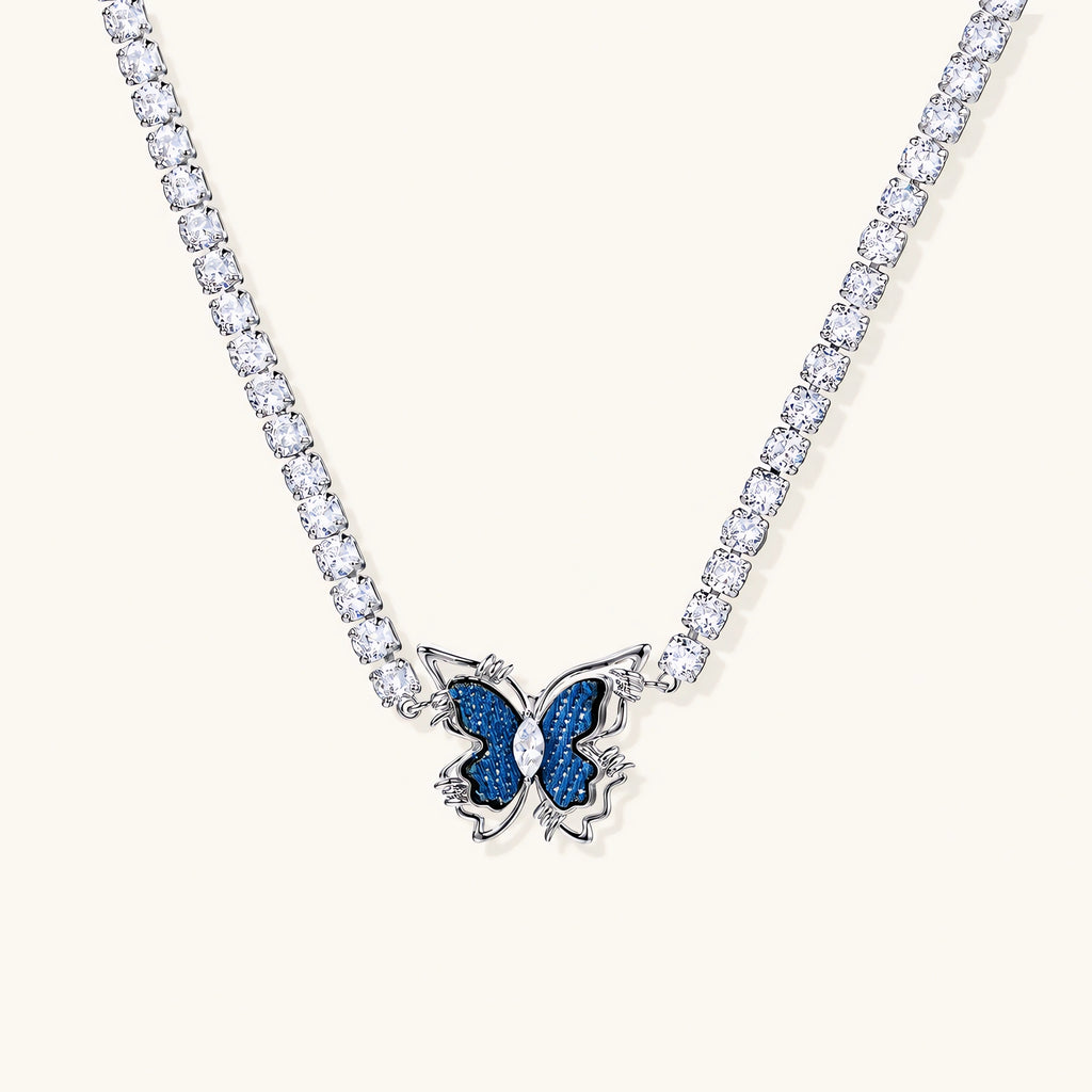 White gold plated tennis necklace with blue denim butterfly pendant and clear zirconia stones on cream background
