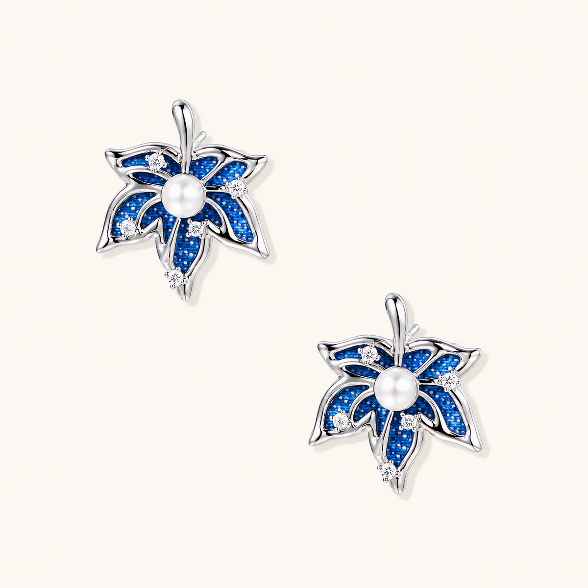 Pair of maple leaf stud earrings with blue denim fabric, a white bead center and zirconia accents in white gold plated eco-brass.