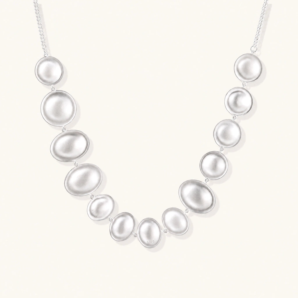 Sterling silver necklace with fourteen matte concave round and oval discs on a curb chain with an adjustable extender.