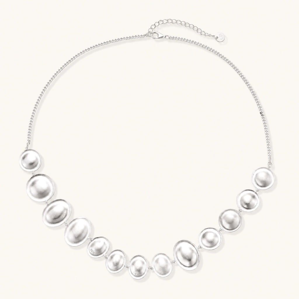 Sterling silver necklace with fourteen matte concave round and oval discs on a curb chain with an adjustable extender.
