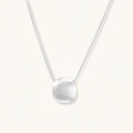 Minimalist brushed sterling silver dome pendant on delicate chain against cream background, showing matte textured finish