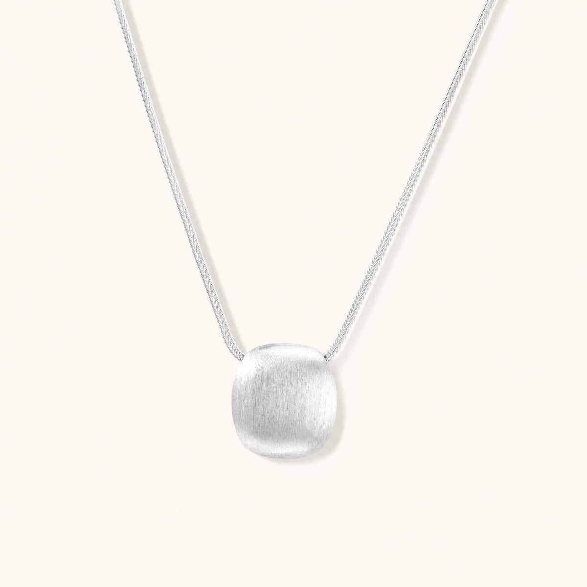 Minimalist brushed sterling silver dome pendant on delicate chain against cream background, showing matte textured finish