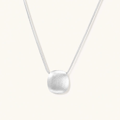 Minimalist brushed sterling silver dome pendant on delicate chain against cream background, showing matte textured finish