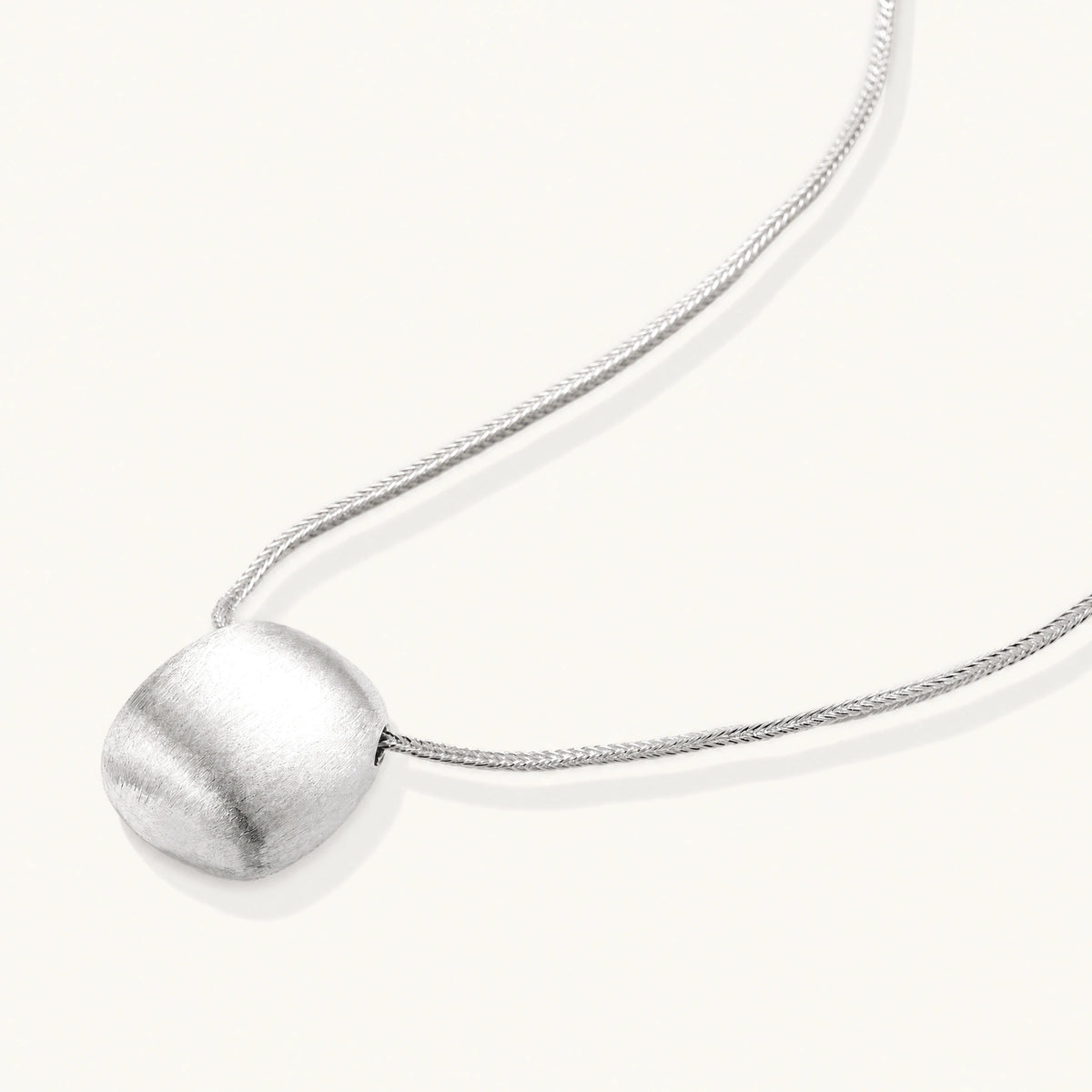 Minimalist brushed sterling silver dome pendant on delicate chain against cream background, showing matte textured finish