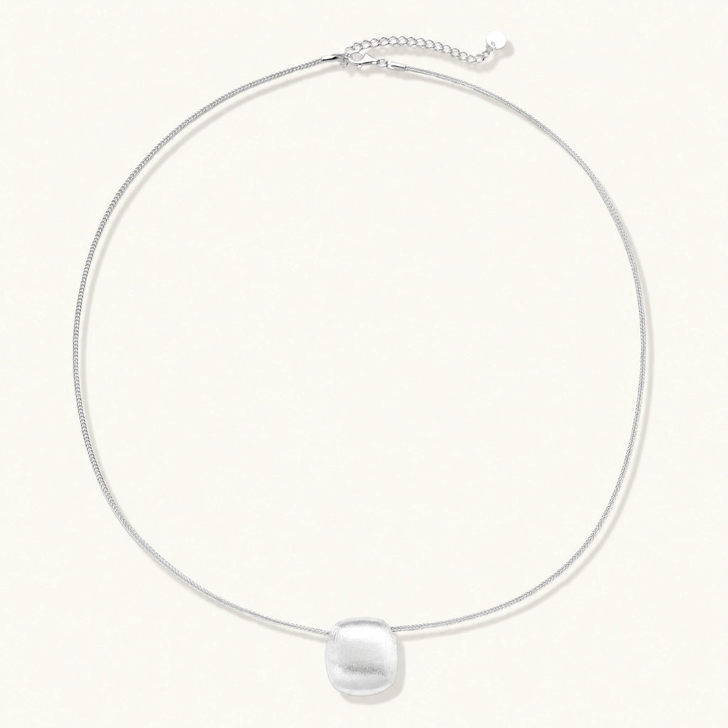 Minimalist brushed sterling silver dome pendant on delicate chain against cream background, showing matte textured finish