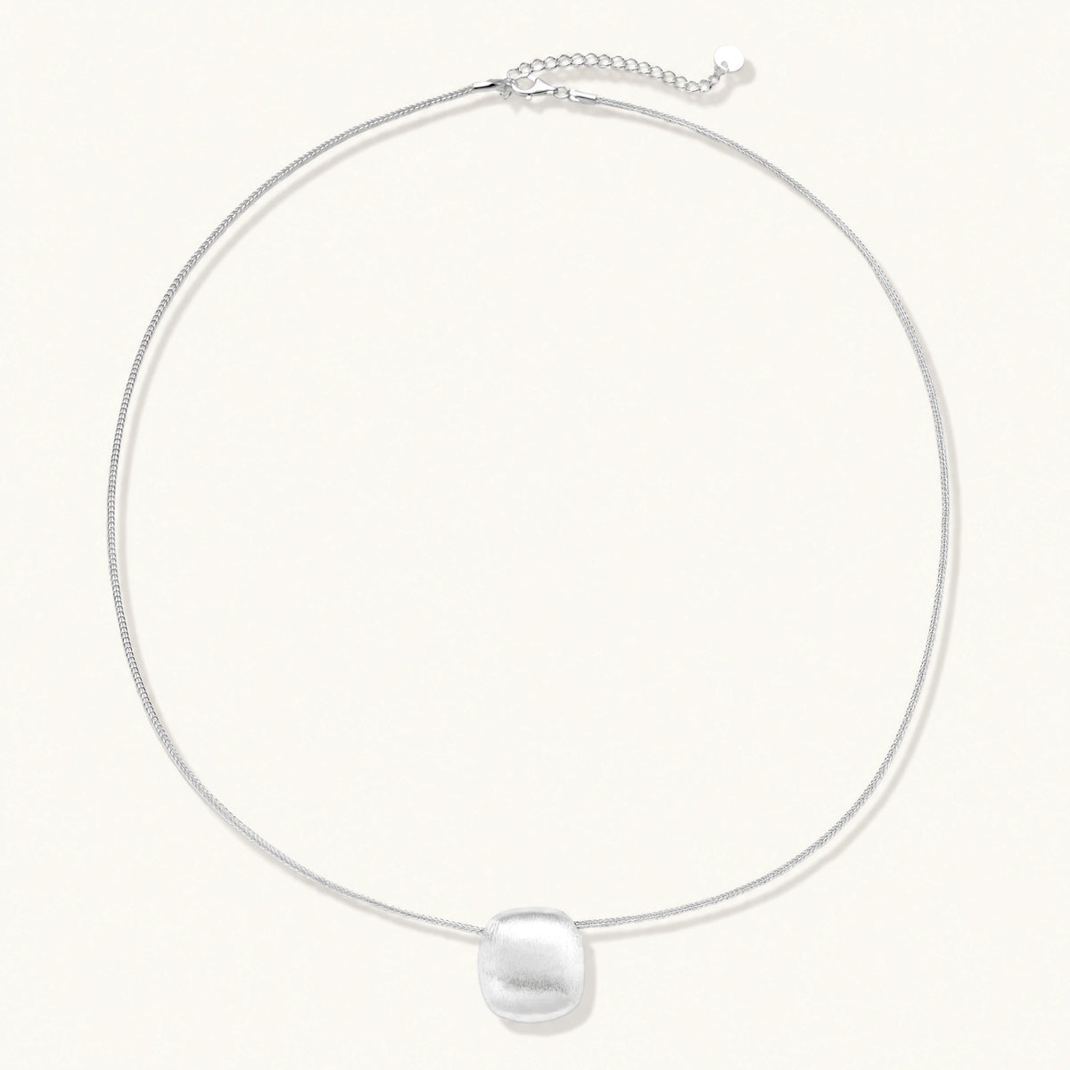 Minimalist brushed sterling silver dome pendant on delicate chain against cream background, showing matte textured finish
