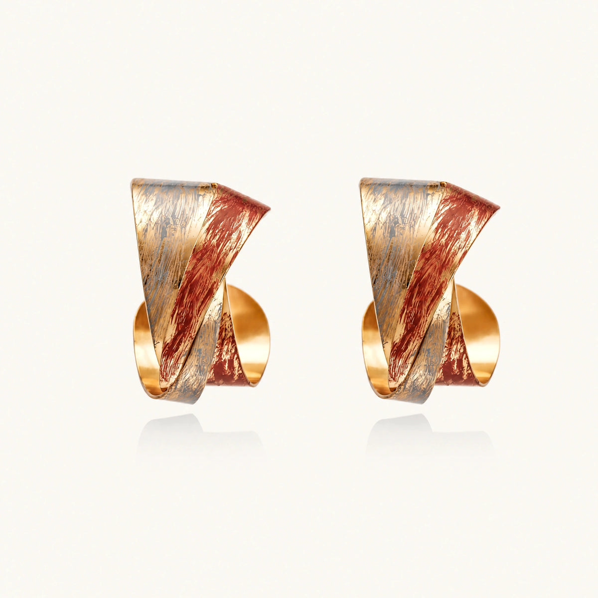 Sculptural gold-plated hoop earrings with diagonal purple and coral enamel stripes in twisted ribbon design
