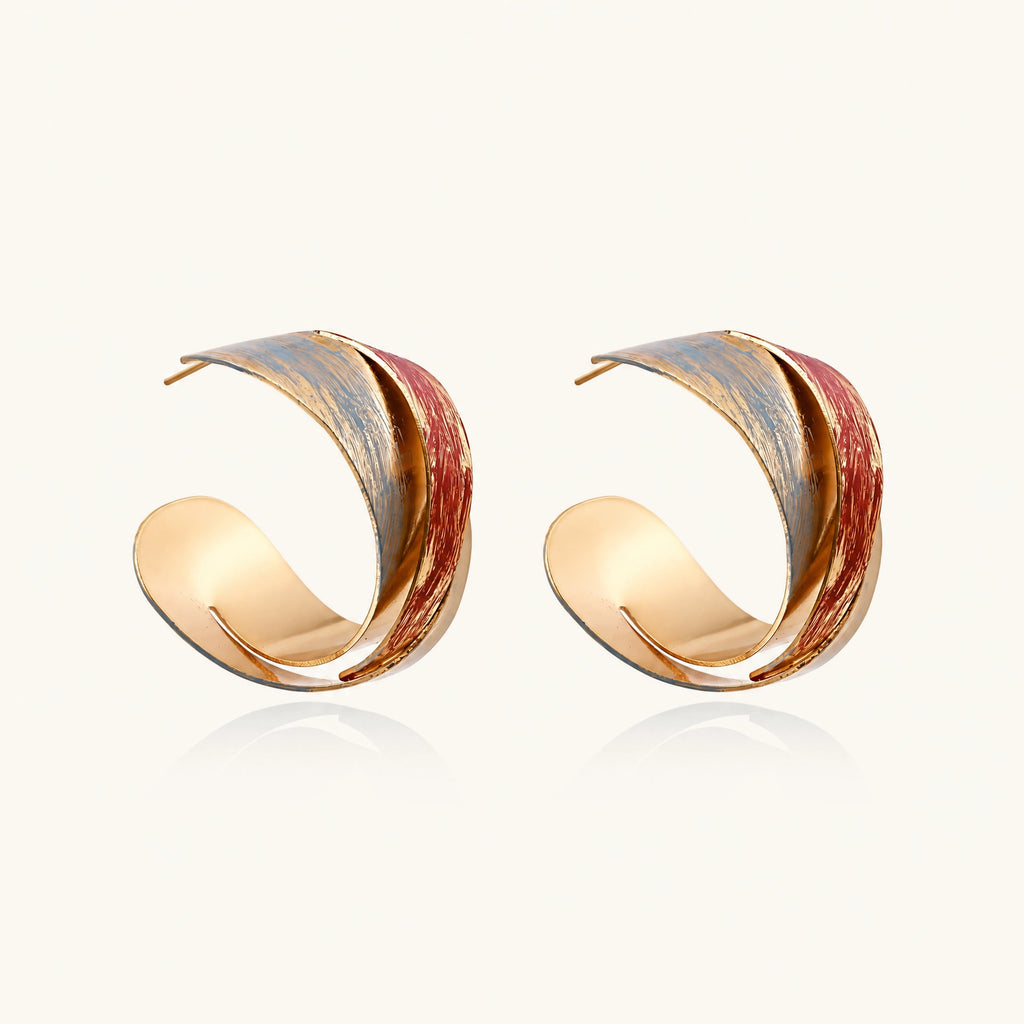Sculptural gold-plated hoop earrings with diagonal purple and coral enamel stripes in twisted ribbon design