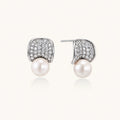 Pair of white gold plated eco-brass stud earrings with curved sparkling stone panels and round freshwater pearls on a cream background.
