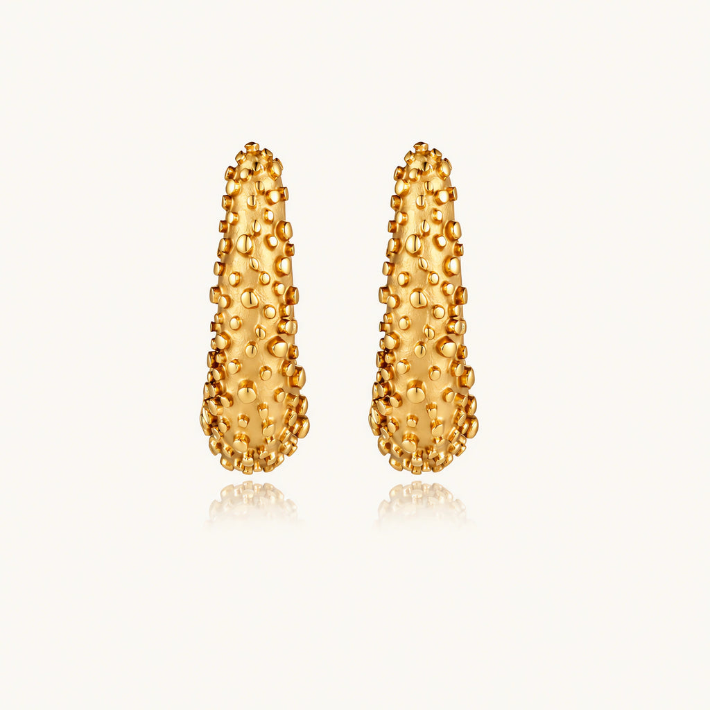 Curved gold hoop earrings with raised granulated texture resembling sea urchin surface on cream background