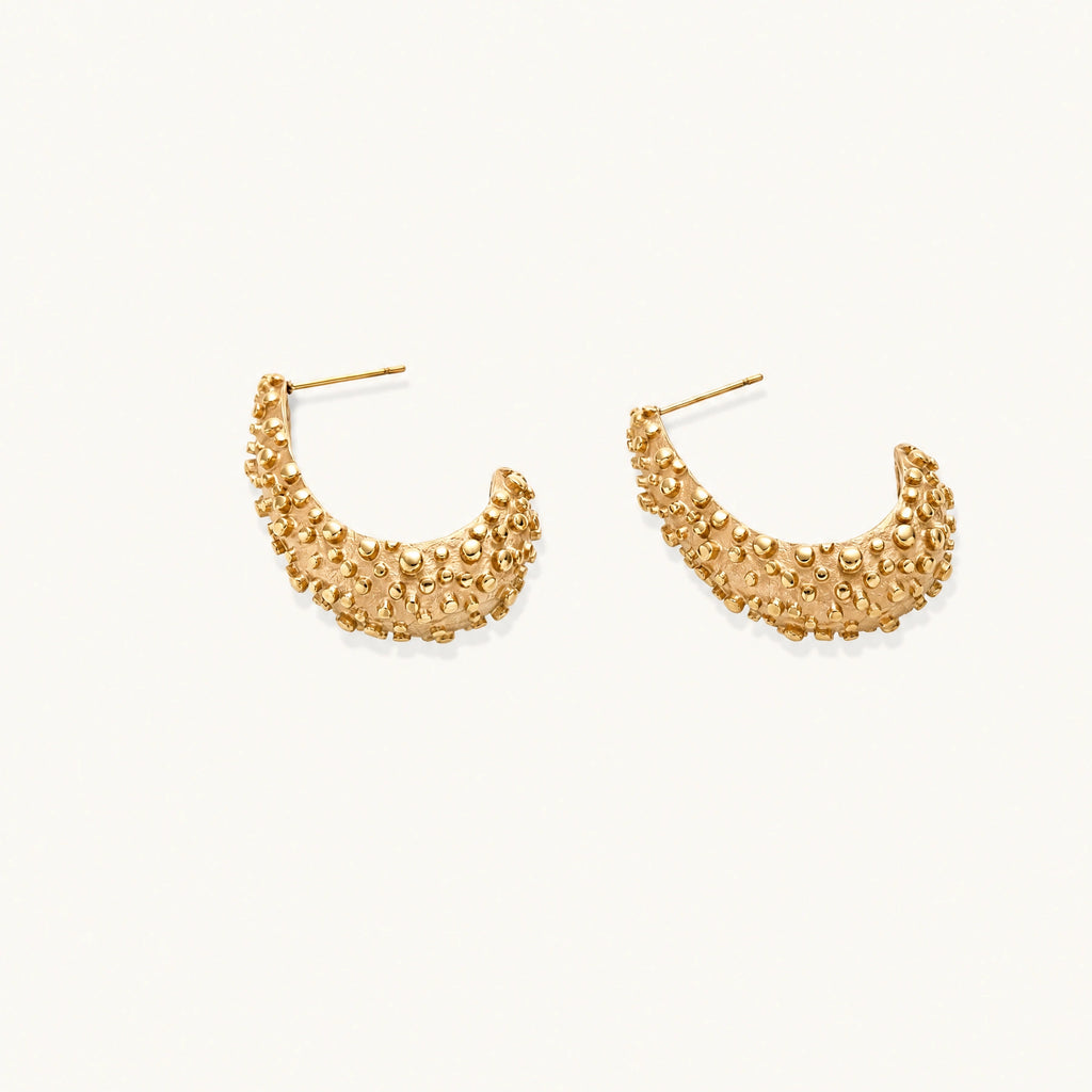 Curved gold hoop earrings with raised granulated texture resembling sea urchin surface on cream background