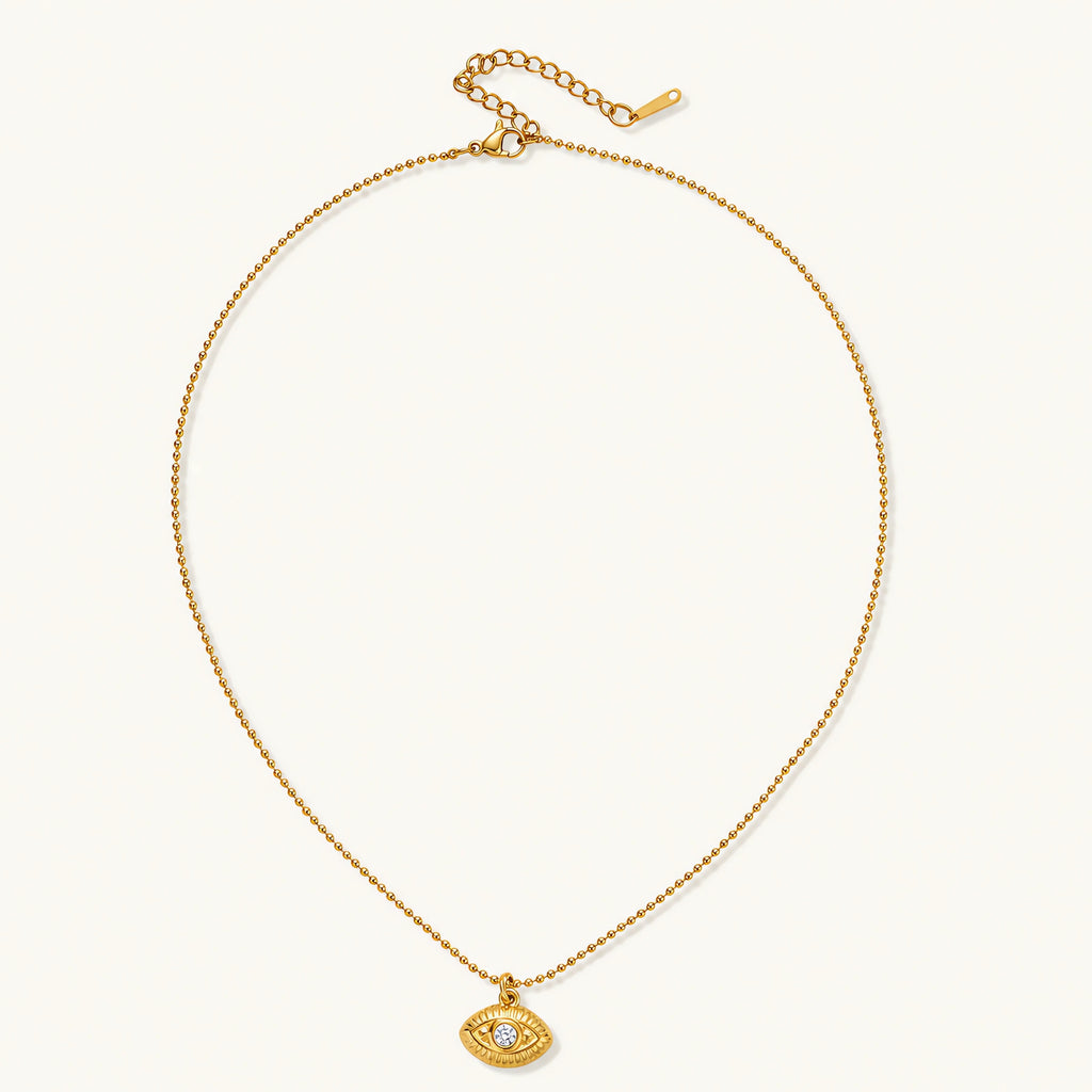 Layered necklace with green stone beads, gold spacers, white accents, and protective eye pendant on cream background.