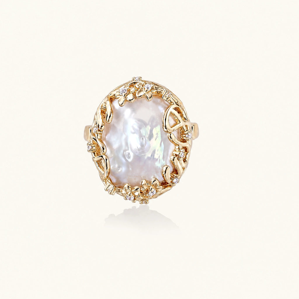 Gold filigree crown ring cradling an iridescent baroque freshwater pearl with crystal accents on white background