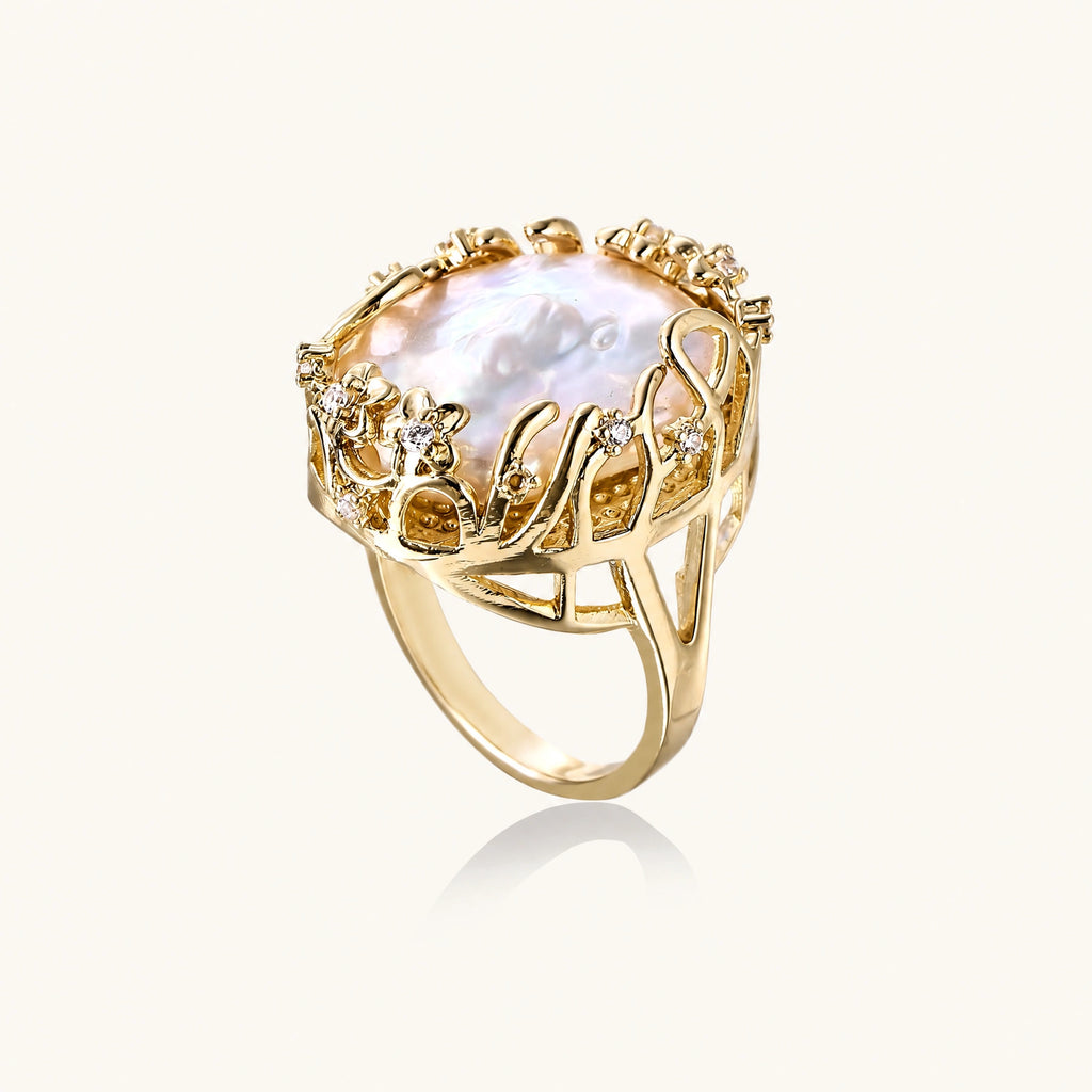 Gold filigree crown ring cradling an iridescent baroque freshwater pearl with crystal accents on white background
