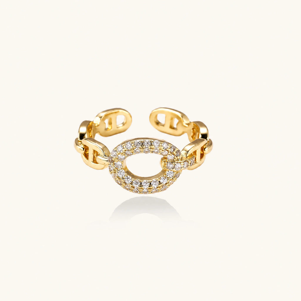 Gold-plated brass chain link ring with one oval CZ-pavé segment on cream background, adjustable cuff style.